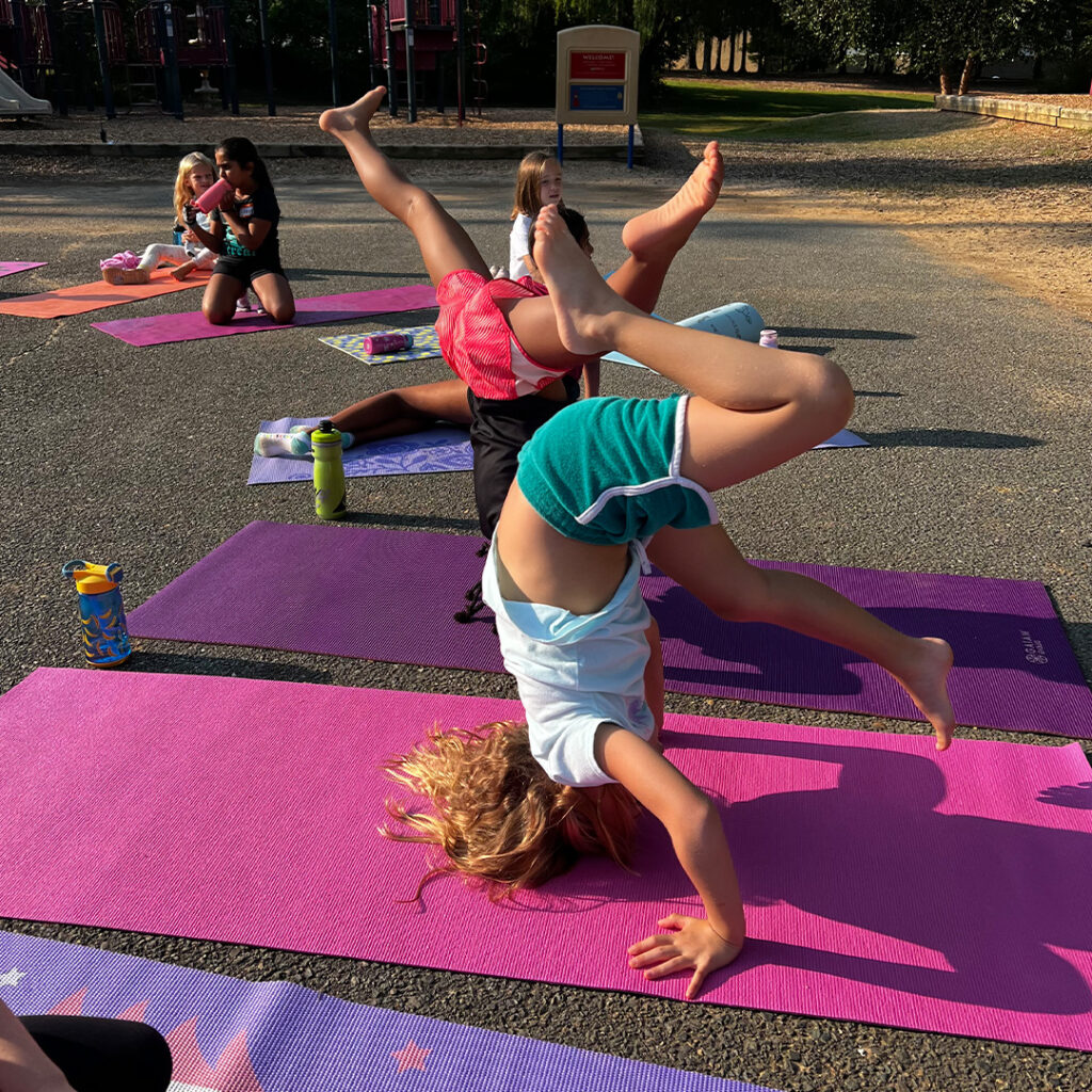Children practicing yoga poses on colorful mats during the Kids Yoga Club Fall Series at Lost Art Yoga, with a focus on active engagement and fun in an outdoor setting.